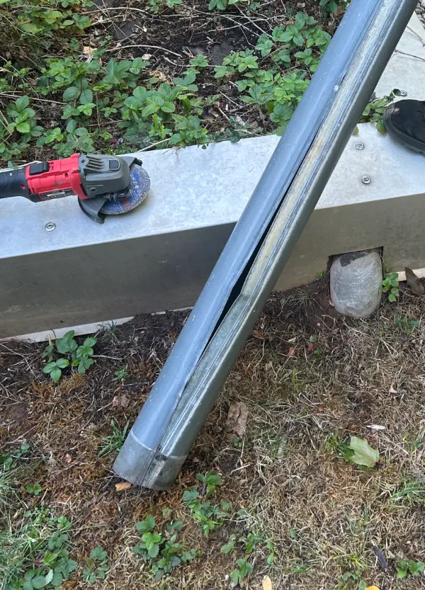 Das ausgebaute alte Fallrohr mit durchgehendem Längsriss, daneben der Winkelschleifer